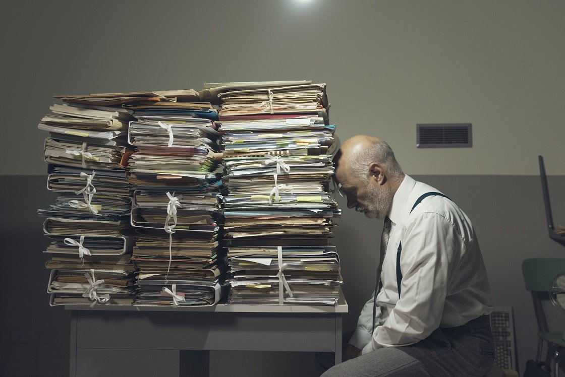 Desperate businessman leans on pile of folders on his desk.