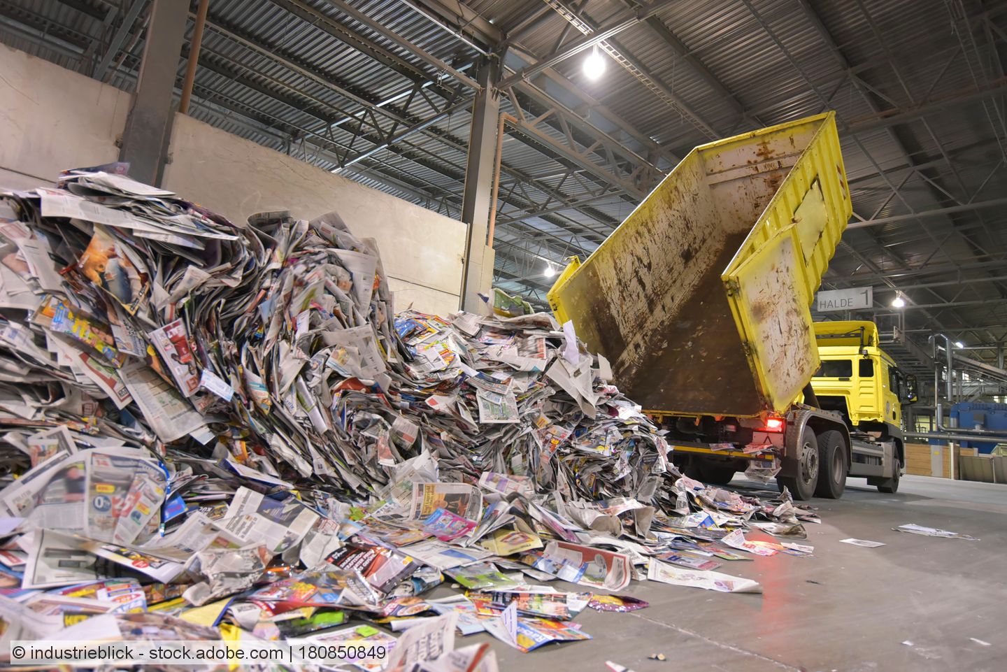 Yellow tipper truck empties old newspapers onto a warehouse floor, stockphoto